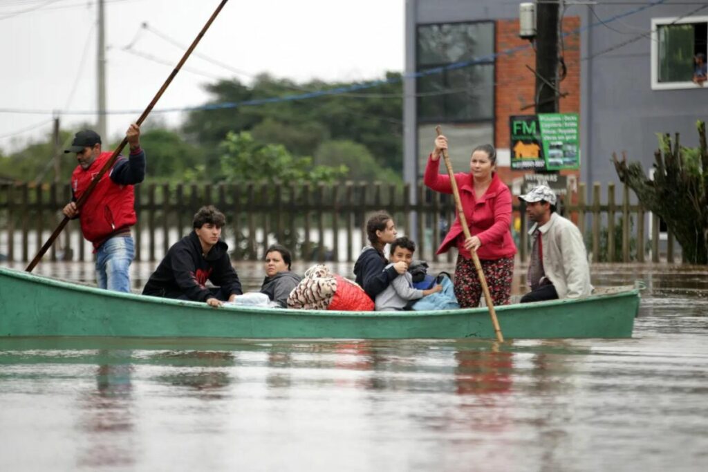 Varias personas esperan junto a unos vehículos atrapados en una zona inundada por las lluvias, en Porto Alegre (Brasil).