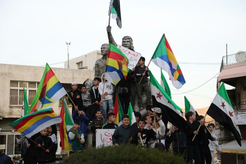 Los partidarios de la oposición siria ondean su bandera y la bandera drusa mientras celebran la toma rebelde de Damasco, en la aldea de Majdal Shams.