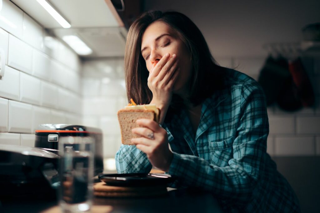 Mujer joven sostiene un sándwich con gesto pensativo, símbolo de ansiedad alimentaria y estrés crónico relacionado al cortisol.