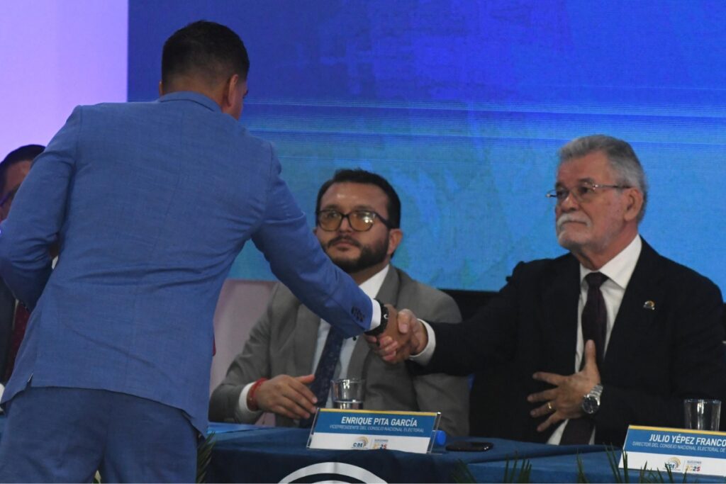 El asambleísta electo, Jaime Estrada (RC), de espaldas, saludando con el consejero del CNE, Enrique Pita.