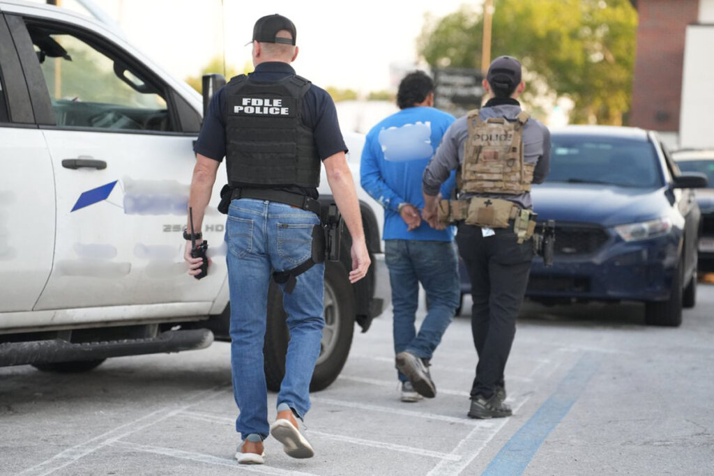Fotografía cedida por el Departamento de Aplicación de la Ley de Florida (FDLE) de agentes de la policía trasladando a un inmigrante detenido durante la operación 'Marea Negra'.