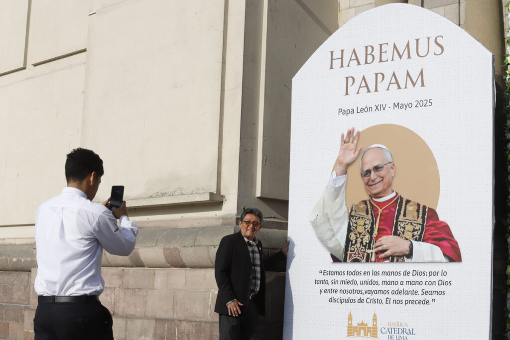 Personas se toman fotografías al lado de una imagen del nuevo Papa León XIV, este viernes en la entrada de la Catedral de Lima (Perú).