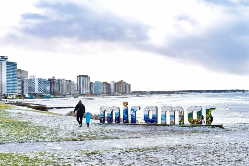 Personas caminan en una playa cubierta de nieve, en Miramar (Argentina).