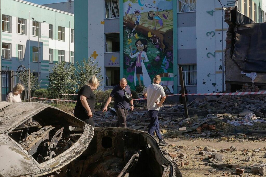 Personas caminan en una zona dañada con autos destruidos cerca de un edificio escolar después de un ataque aéreo ruso en Kiev, Ucrania.